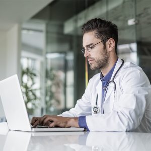 Male doctor using laptop at desk in clinic Confident male doctor using laptop at desk in clinic. Medical professional is wearing lab coat. He is working on computer.